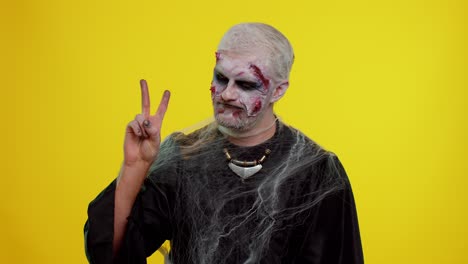 halloween hombre zombi maquillaje sangriento mostrando el signo de la victoria, con la esperanza de éxito y ganar el gesto de paz
