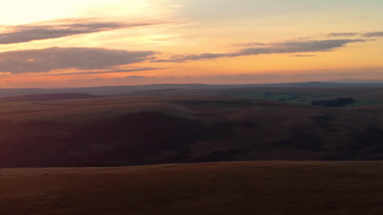 Moving and Panning Aerial Shot of Wind Farm at Sunset to Reveal Incredible Sunset Through Clouds on Horizon with Rolling Welsh Countryside Hills and Open Landscape near Swansea, Wales 4K