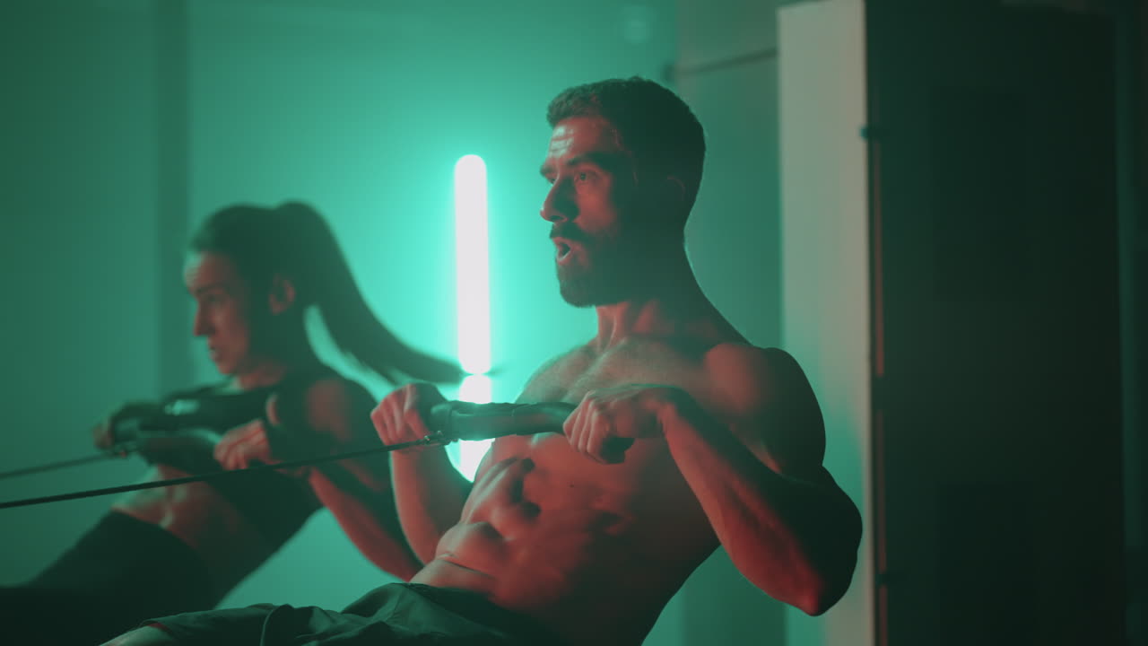 cámara lenta: hombre y mujer entrenando en una máquina de remo en el gimnasio