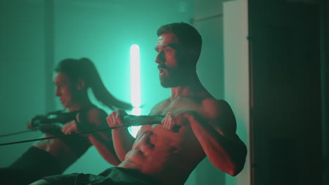 cámara lenta: hombre y mujer entrenando en una máquina de remo en el gimnasio
