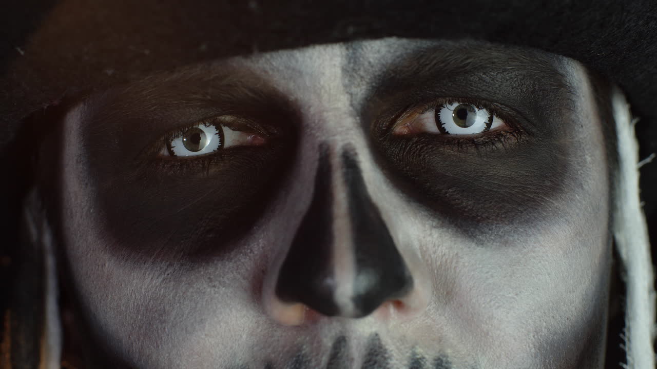 Close-up shot of face in skeleton Halloween makeup opening eyes with white pupil, trying to scare
