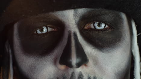 Close-up-shot-of-face-in-skeleton-Halloween-makeup-opening-eyes-with-white-pupil,-trying-to-scare