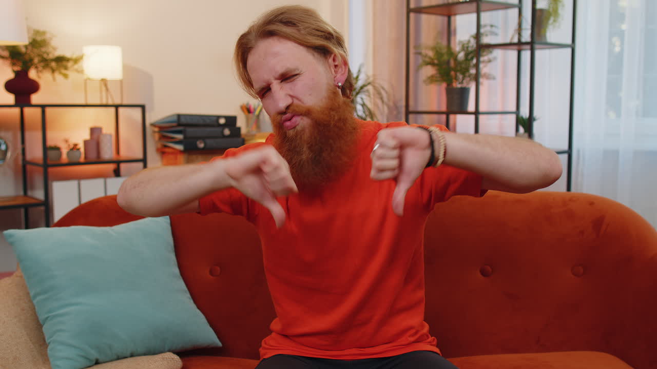 화가 난 젊은 남자가 엄지손가락을 내려놓고, 나쁜 일을 싫어하고, 승인하지 않고, 집에서 불만족스러운 피드백을 합니다.