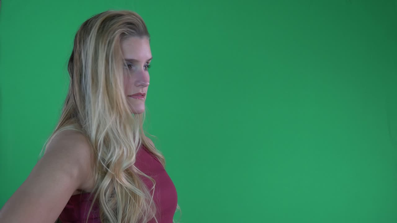 Bela Mulher Loira com Regata Vermelha Joga o Cabelo e Posa para a Câmera em Frente a uma Tela Verde.
