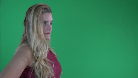 beautiful blonde woman in red tank top flips hair and poses for camera in front of green screen