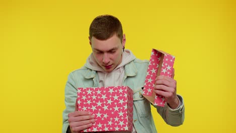 young man unwrapping birthday gift and expressing disappointment, dislike bad present, dissatisfied