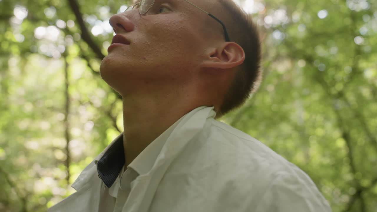 Portrait view of man adjusting and putting on white lab coat in forest, surrounded by greenery and natural light, highlighting preparation, outdoor lifestyle, concentration, and scientific context