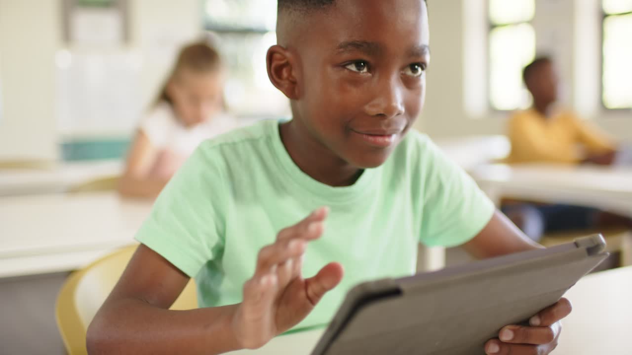 African American male child student tapping, scrolling tablet at desk, finishing task and smiling