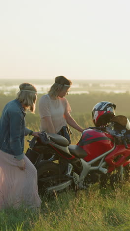 dos hermanas limpian alegremente una motocicleta roja en un campo abierto de hierba al atardecer, una hermana baila mientras sostiene su bata