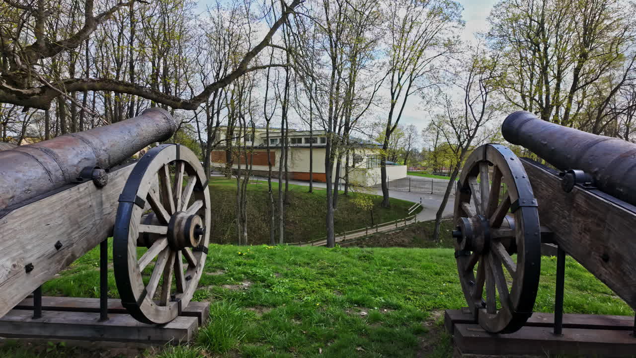 Cast iron cannon in wooden recreation support beams with wheels for recoil displayed on hilside under trees