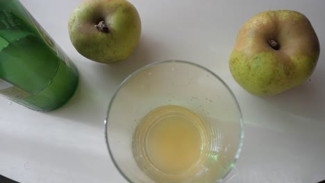 fresh natural cider being poured into a glass, with apples visible in the background