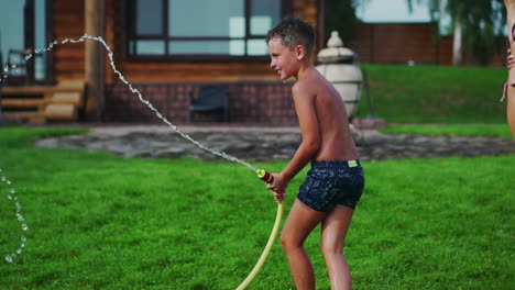 mother with father and two children playing on the lawn pouring water laughing and having fun on the playground with lawn on the background of his house near the lake in slow motion