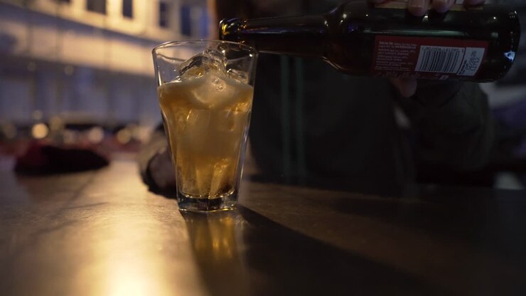 Primo piano di una ragazza che versa sidro o birra in un bicchiere pieno di ghiaccio in un club-bar di sera.