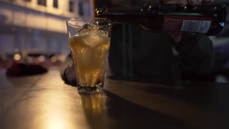 closeup of a girl pouring cider or beer in a glass full of ice in a club-bar in the evening