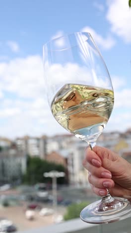 woman holding a glass of white wine outdoors with city view