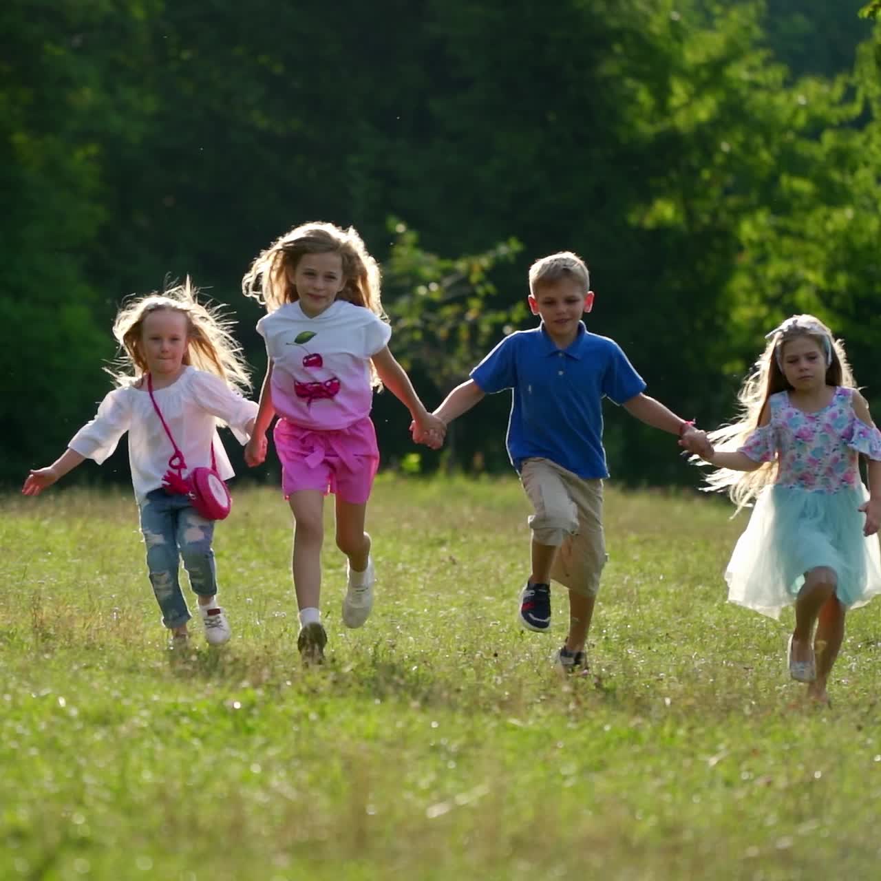 Children run outside in park on green grass. Cute kids holding hands while having good mood in park. Sunny summer day outside