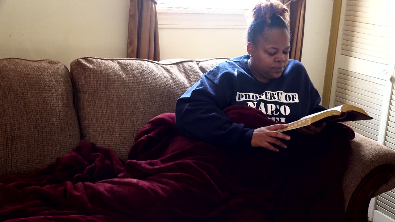 donna afroamericana che legge la bibbia mentre si sdraia sul divano