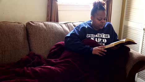 mujer afroamericana leyendo la biblia mientras descansa en el sofá