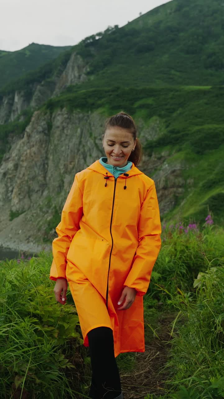 Happy Woman in Orange Raincoat Standing in Green Mountain Landscape