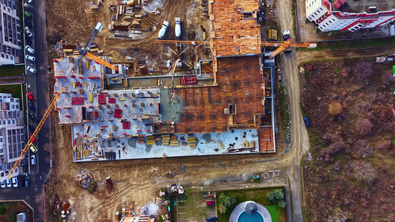 Eine Baustelle, die den Baufortschritt mit Kränen, LKWs und Geräten in der Nähe eines Poolbereichs und offenem Gelände in einer wachsenden Community an einem klaren Tag zeigt