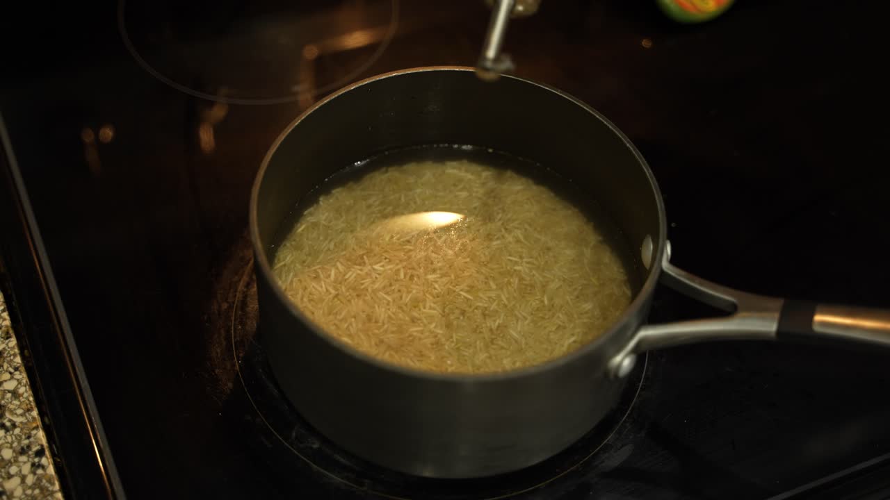 Riso e fagioli che sobbollono in una casseruola con olio su un fornello in una cucina domestica.