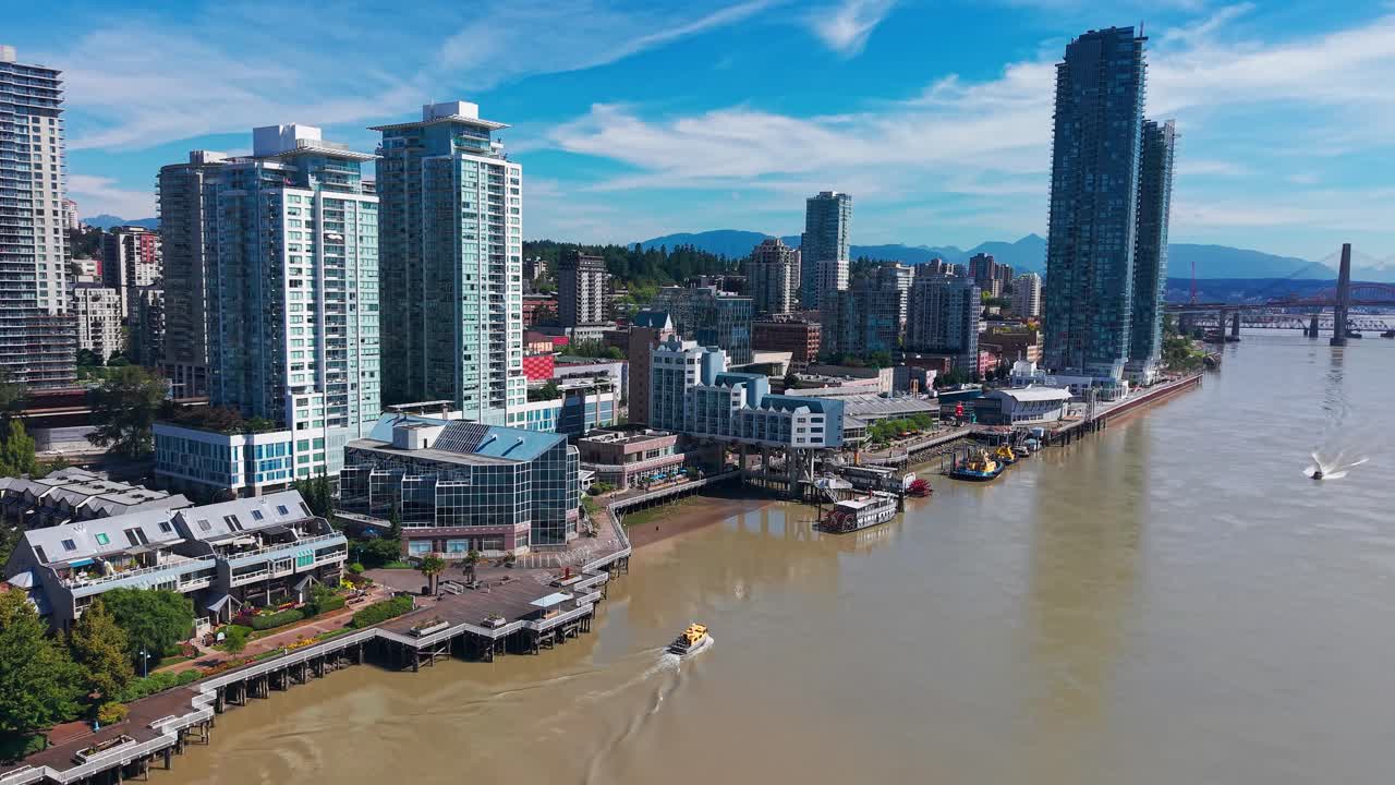 Filmato aereo di droni di imbarcazioni che navigano lungo il fiume Fraser oltre il moderno skyline di New Westminster, nella Columbia Britannica, con grattacieli e il Pattullo Bridge sullo sfondo