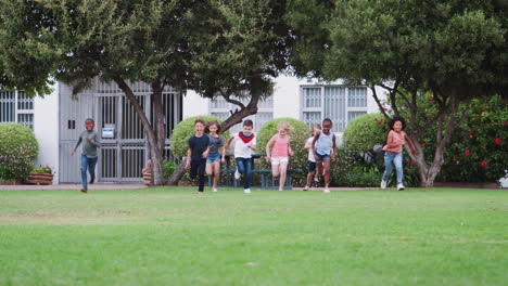 group of excited children playing with friends and running across grass playing field