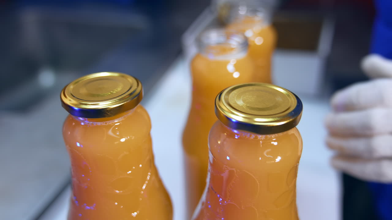 Food factory worker's hands in gloves put the caps on the bottles. Fresh apple juice in bottles being shut close up.