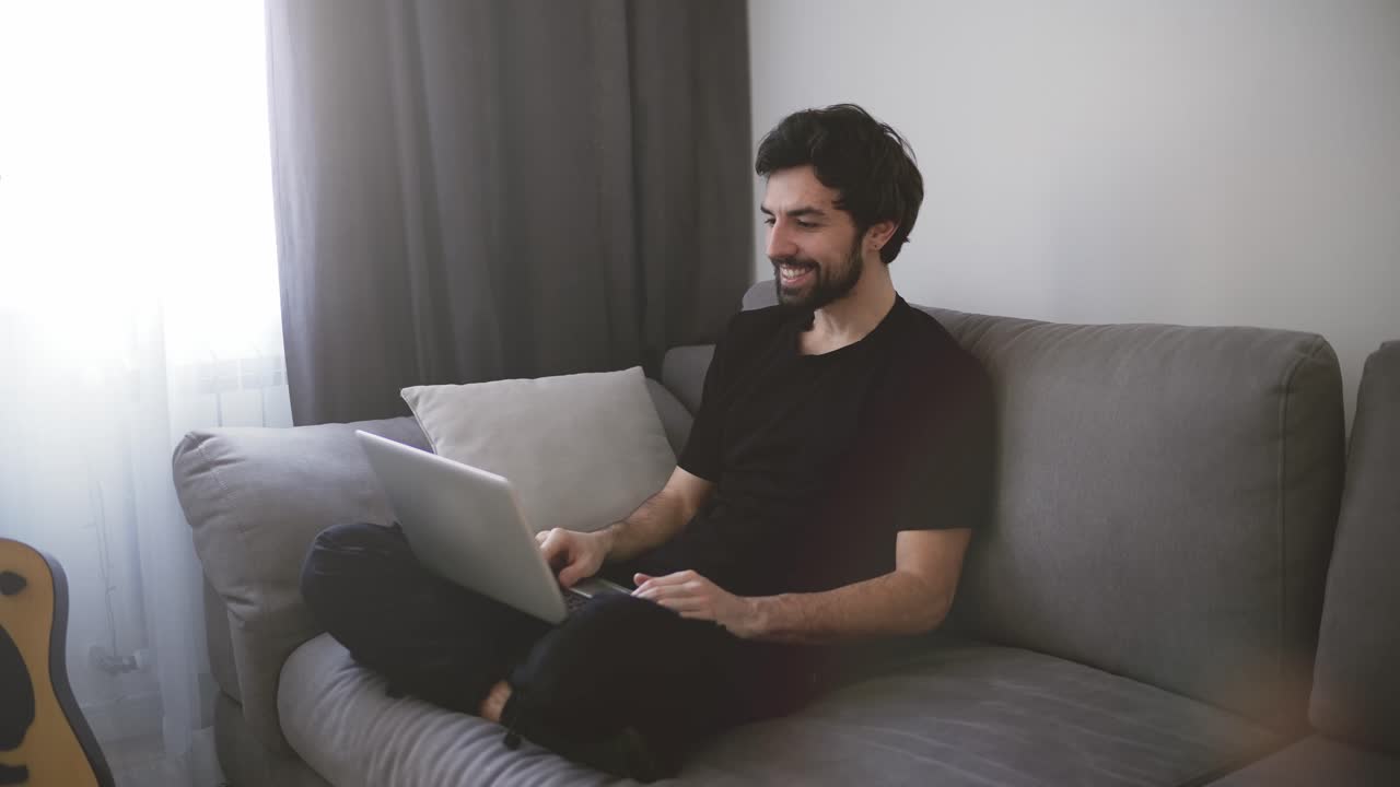 hombre feliz relajándose en el sofá mientras hace videollamadas usando una computadora portátil en casa