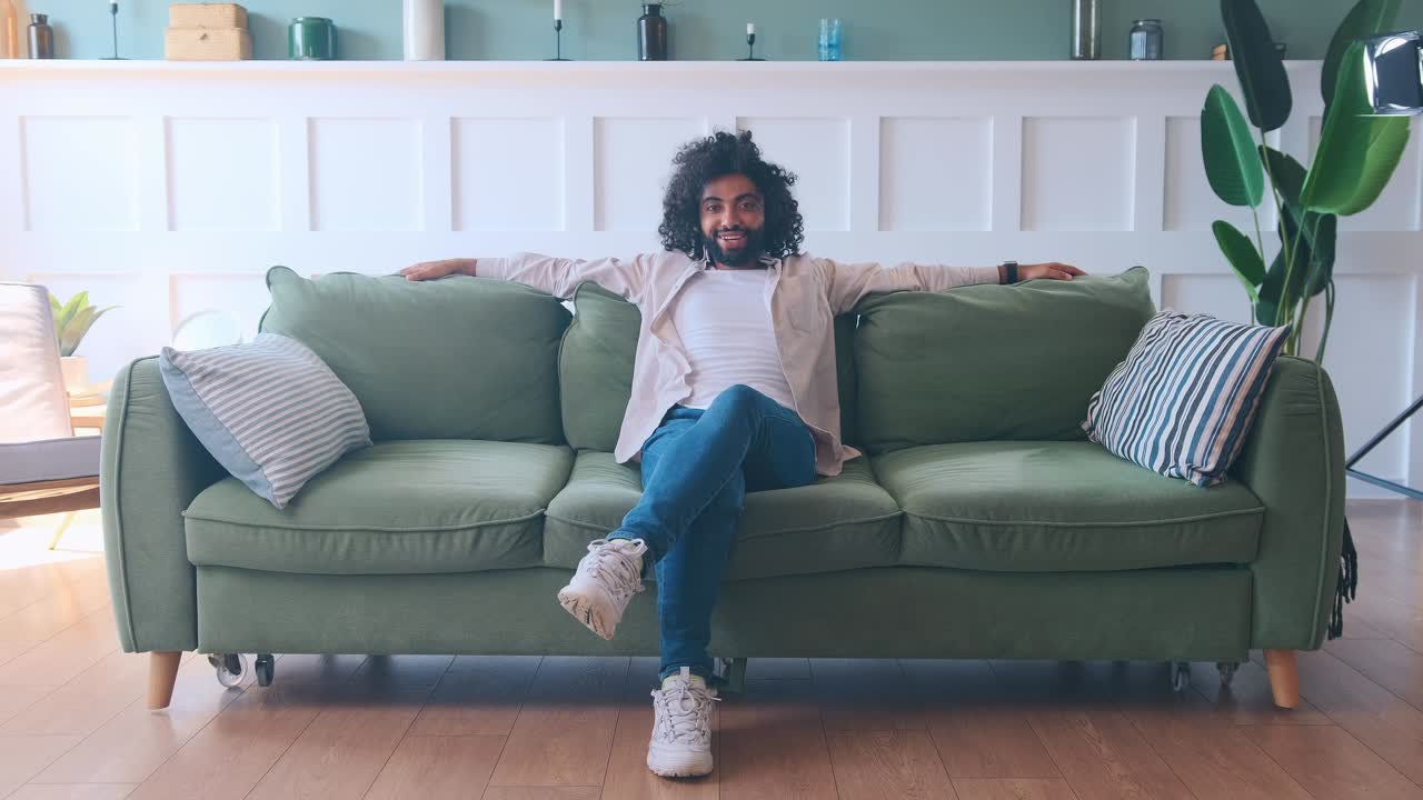 Young successful arabian man crosslegged posing on large sofa in living room