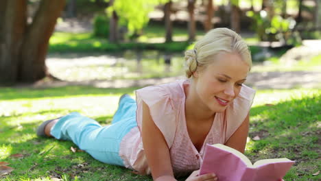 una mujer se acuesta en el parque leyendo mientras mira a la cámara