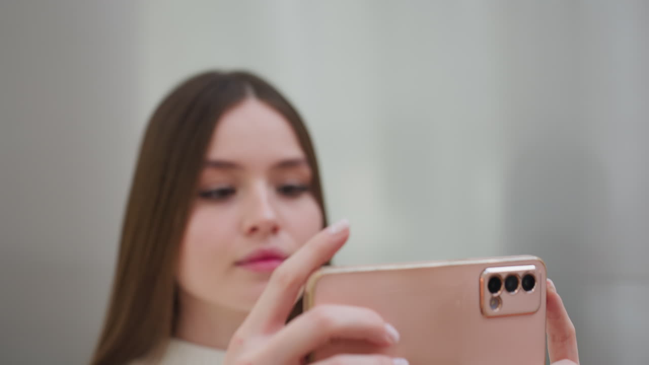 Close-up of woman taking selfie with smartphone, slightly blurred face, well-manicured hands holding phone in stylish modern setting, elegant nails, soft lighting, neutral background
