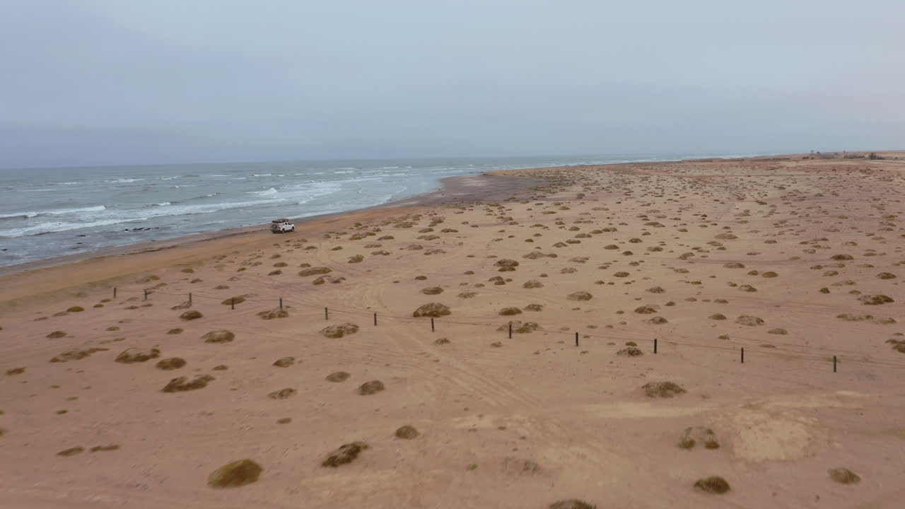 Drone follows a lone SUV driving on a vast, empty beach near Swakopmund on a moody, overcast day