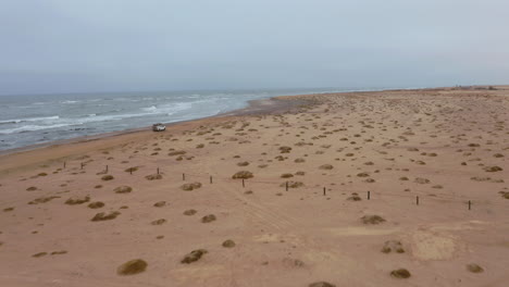 drone follows a lone suv driving on a vast, empty beach near swakopmund on a moody, overcast day