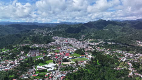 aerial timelapse view of chichicastenango, guatemala, with dense town buildings nestled in lush green mountains under scattered clouds