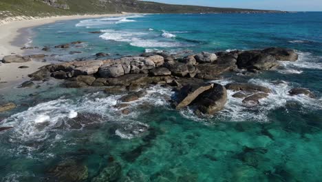 Aerial-view-flying-backwards-over-rocks-in-empty-beach-with-turquoise-water-and-white-sand