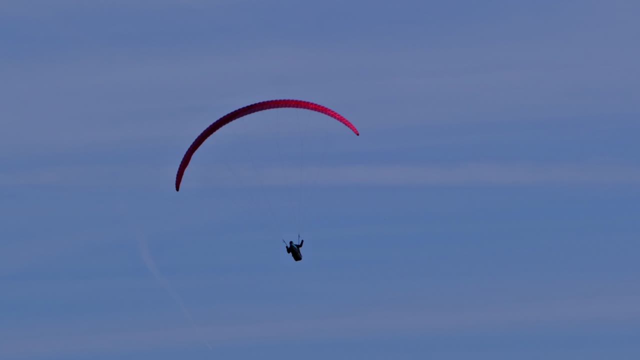 Bottom view of paraglider with red parachute flying circes on a bright blue sunny day