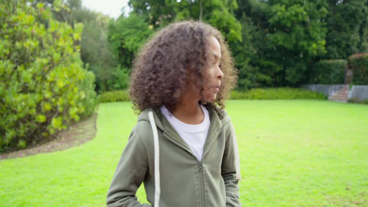 Elementary school boy in hoodie on backyard observing hedge turning to camera, smiling to greet