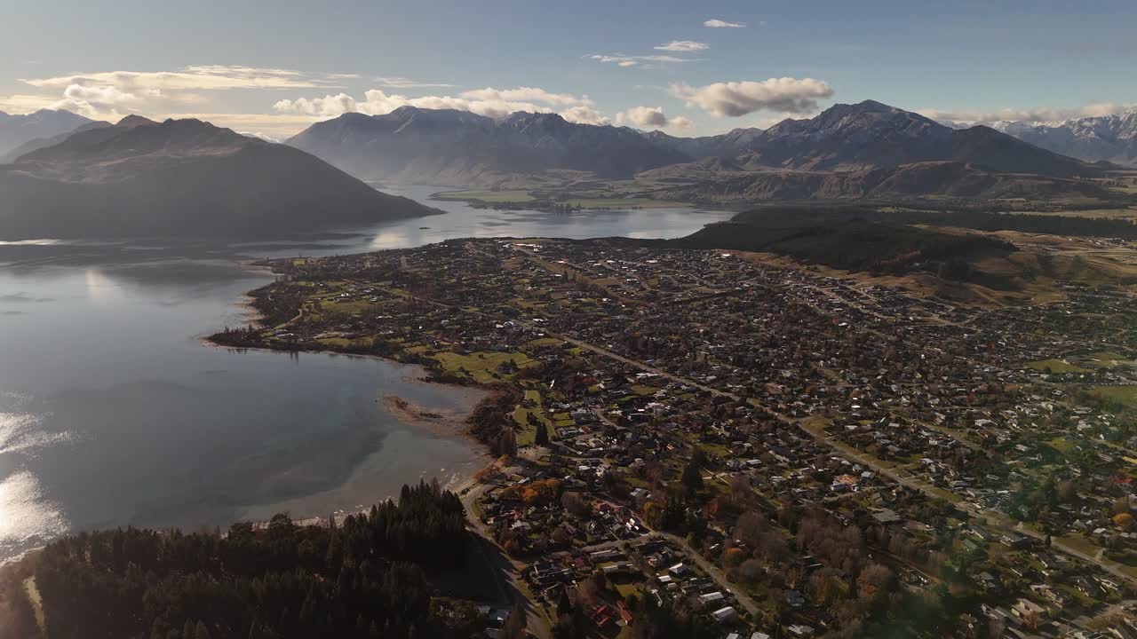 Picturesque landscape of wanaka area in New Zealand. Panorama view of small town, lake and mountains in distance. Foggy sunrise in the morning. Rooftops of homes and houses