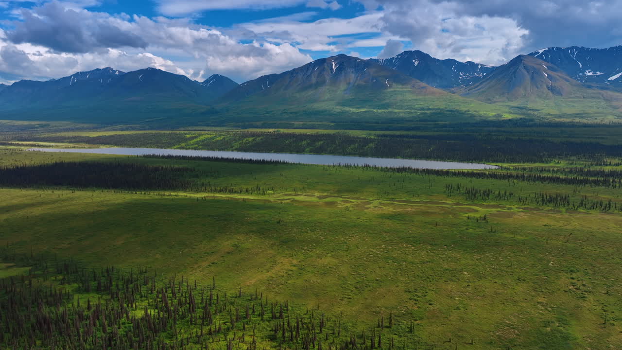 Rising over the vast green valley with long pond. Striking mountains and beautiful clouds above them at backdrop