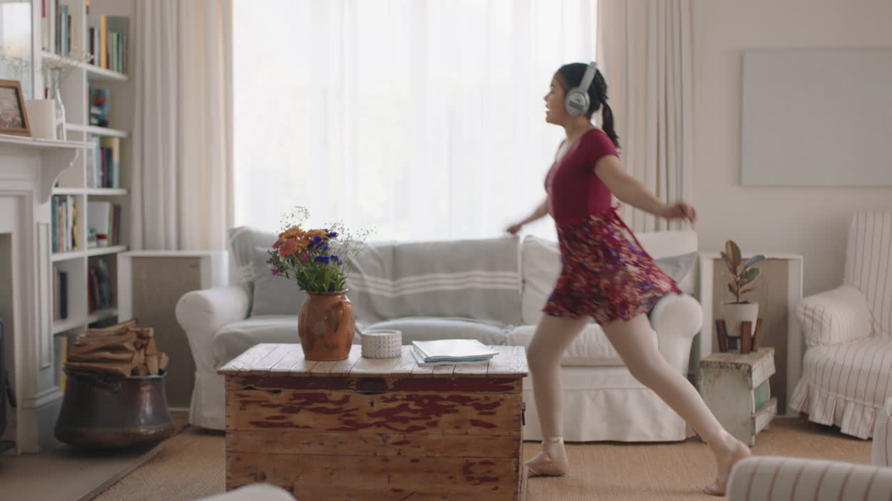 행복한 십대 소녀가 춤을 추고 집에서 발레 춤 동작을 연습하고 음악을 듣고 헤드폰을 착용하고 재미있게 주말을 즐기고 있습니다.