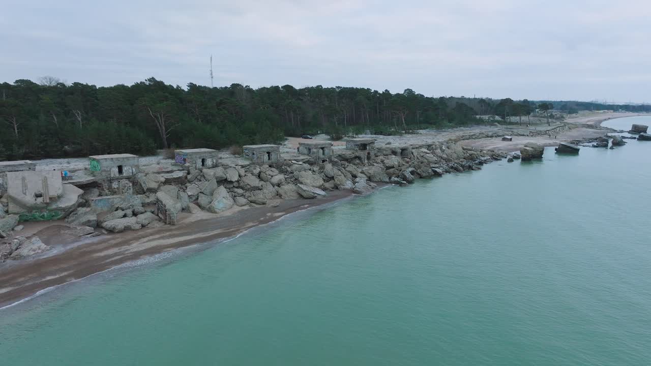 съемка с воздуха заброшенных приморских фортификационных сооружений в северных фортах каросты на берегу балтийского моря, пасмурный день, широкая съемка с дрона, движущаяся вперед