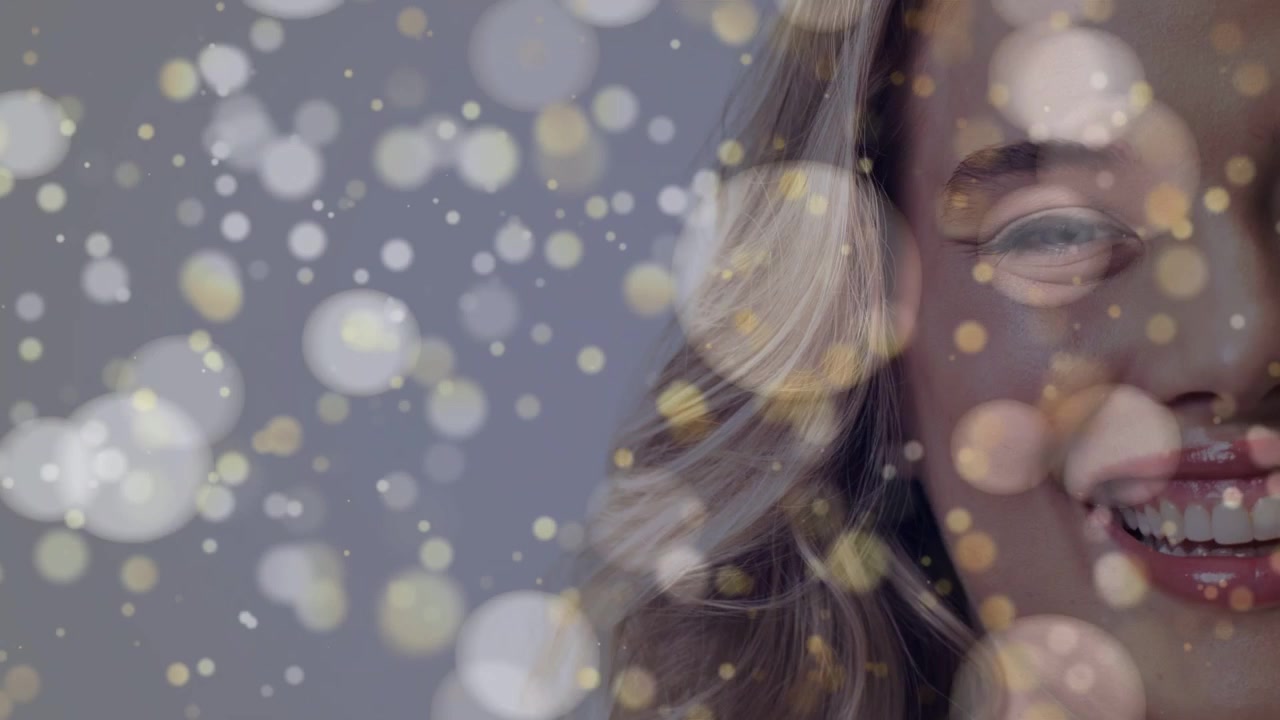 Kvinde smiler i skønhedsportræt, mens et bokeh-overlay driver hen over en grå baggrund og afslører ansigtet.