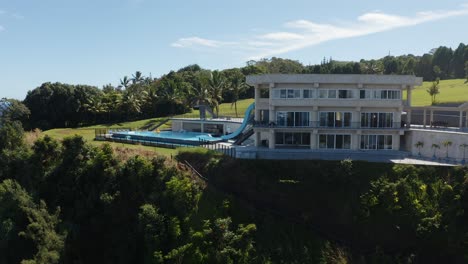 Aerial-shot-of-a-modern-luxurious-private-resort-on-the-side-of-a-cliff-surrounded-by-lush-green-foliage