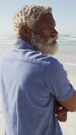 vertical video of senior african american man looking into distance on beach