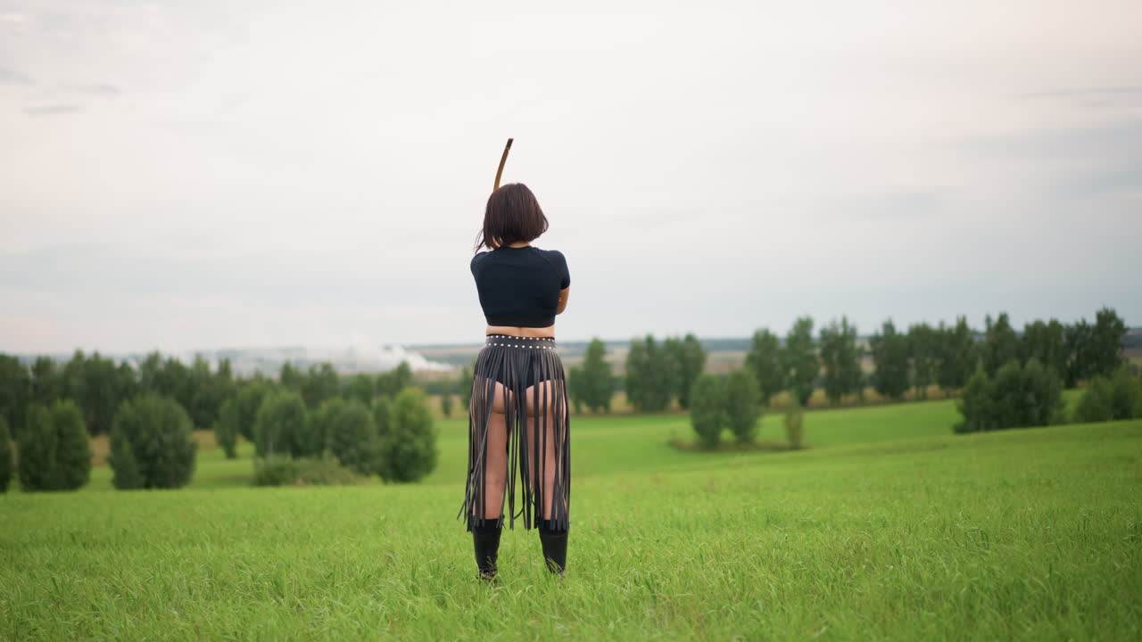 緑の草原に立つ白い肌の女性戦士。革のスカートを身に着け、弓を背に、曇り空の下で並木に向き合っています。孤独と覚悟を示す瞑想的な立ち姿で、斥候が地平線を監視するレンジャーのようです。
