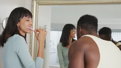 Happy-diverse-couple-looking-in-mirror-and-brushing-teeth-in-bathroom