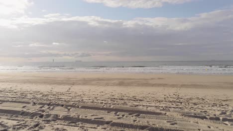 Flying-low-over-a-wrecked-sand-castle-and-footprints,-along-the-North-Sea-coast-Belgium,-aerial