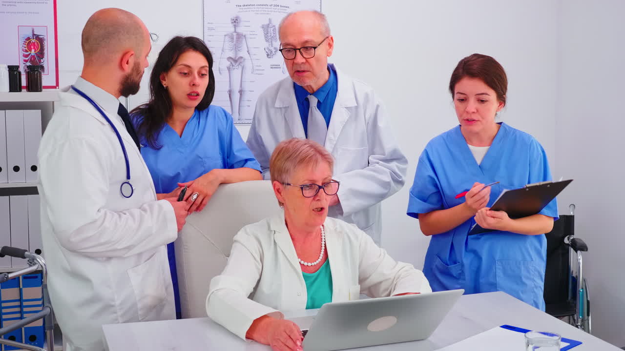 Medical practitoner working on laptop during briefing with coworkers