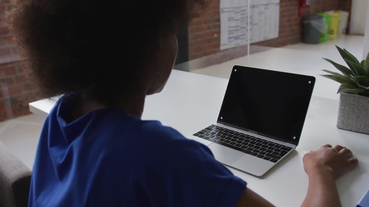 Imprenditrice afroamericana seduta a una scrivania che fa una videochiamata usando un laptop con spazio per il testo.